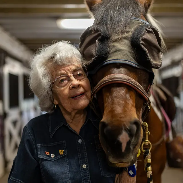 Patricia standing beside a horse in a stable and holding a lead rope / Patricia debout à côté d’un cheval dans une écurie tenant une longe