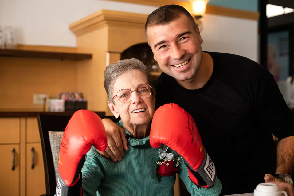 Senior woman wearing boxing gloves smiling and posing together with her favorite boxing star / Femme âgée portant des gants de boxe, souriant et posant avec sa star de boxe préférée