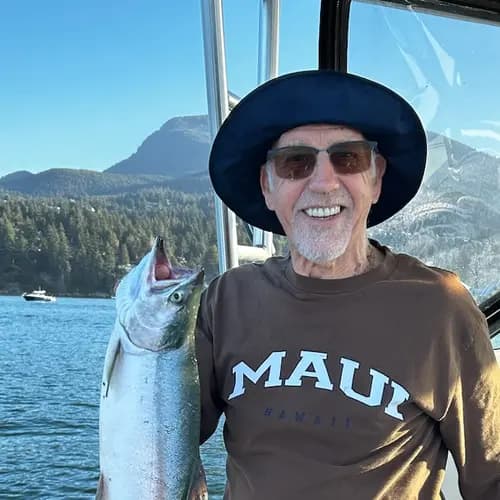Senior man is brightly smiling on a boat while holding a big fish that he caught / Un homme âgé sourit sur un bateau en tenant un gros poisson qu'il a attrapé.