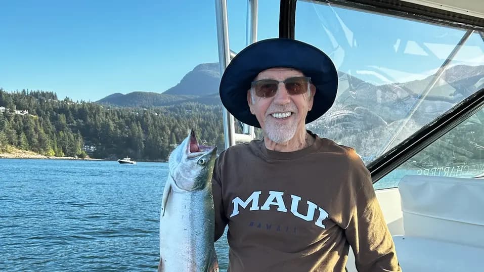 Senior man is brightly smiling on a boat while holding a big fish that he caught / Un homme âgé sourit sur un bateau en tenant un gros poisson qu'il a attrapé.